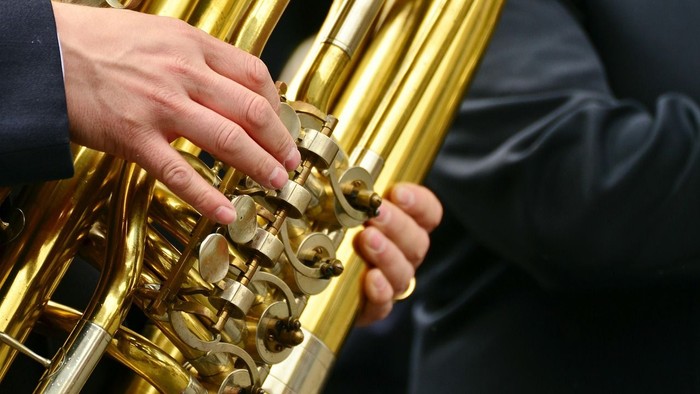 Ausschnitt aus einer Tuba mit den Händen des Spielers.