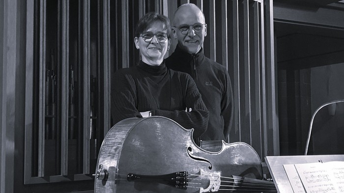 Zwei Musiker posieren mit einem Cello und Notenblättern in einem Konzertumfeld.
