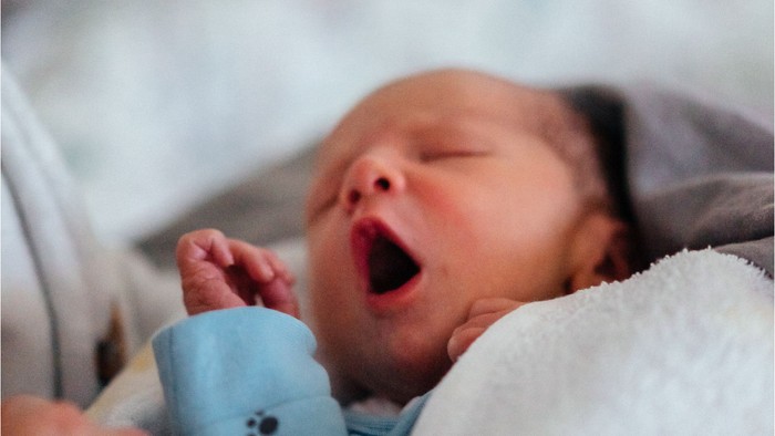 Et spæd barn giver sig til at gylle med en blå flaske i munden.