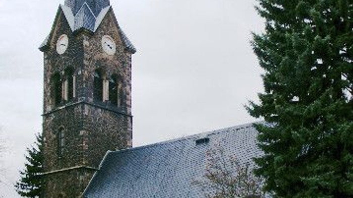 Kirchturm mit Uhr und Friedhof, umgeben von Bäumen