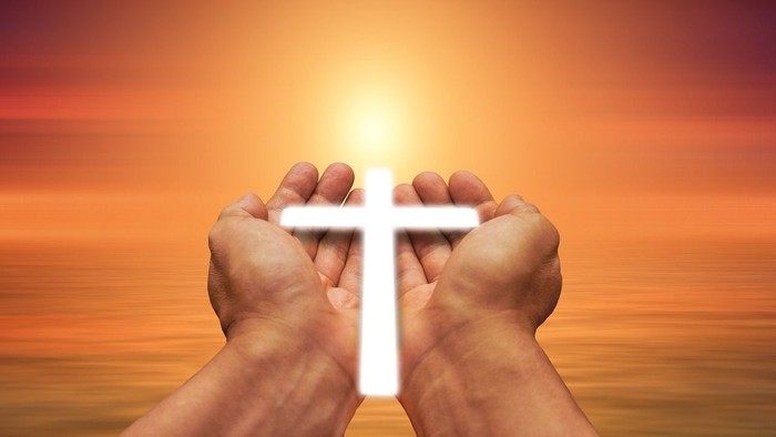 Hände halten Kreuz vor Sonnenuntergang