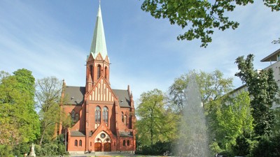 Ein rotes Kirche mit hohem Turm und ein Brunnen im Vordergrund