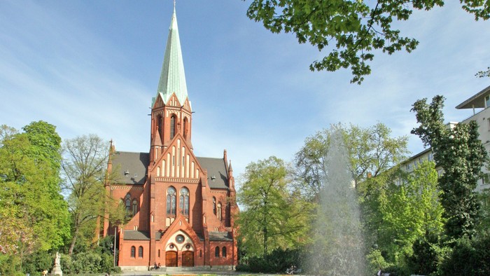 Ein rotes Kirche mit hohem Turm und ein Brunnen im Vordergrund