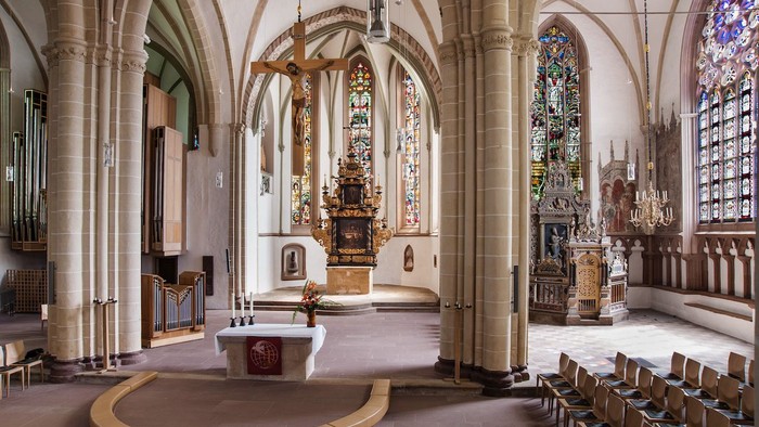 Großzügige Kircheninneraum mit hohen Bögen, bunten Glasfenstern und einem Altar im Mittelpunkt