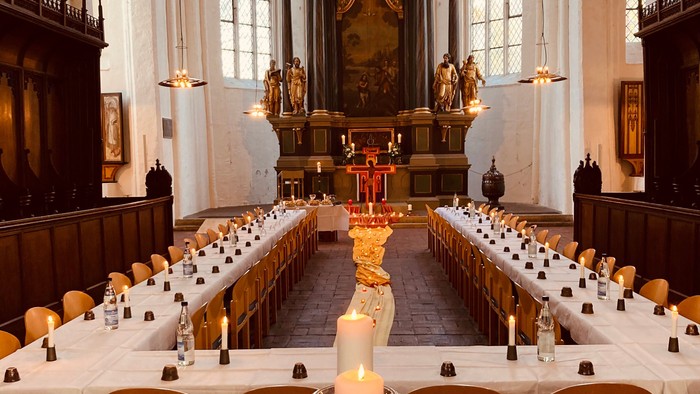 In der Kirche stehen lange Tische mit weißen Tischdecken und Kerzen.