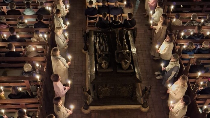 Viele Menschen sitzen in einer Kirche und halten Kerzen