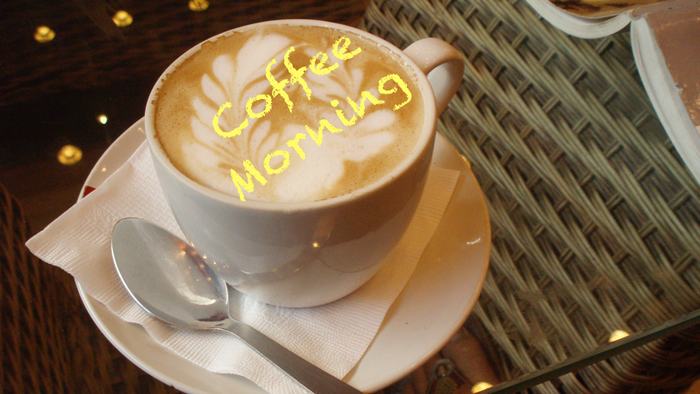 Cup of coffee with "Coffee Morning" written in foam, spoon on saucer