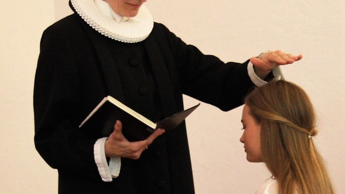 En person i dommerdrægt og med bog taler til en ung kvinde.