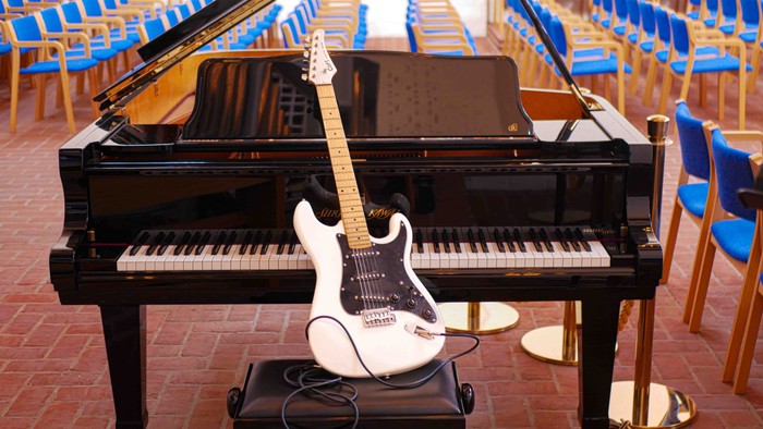 En hvid elektrisk guitar hviler på et sort klaver i en tom auditorium.