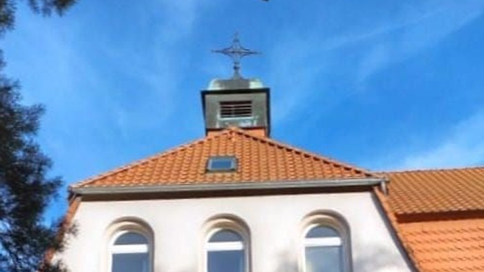 Moderne Kirchengebäude mit Bogenfenstern, rotem Ziegeldach und einem kleinen Glockenturm.