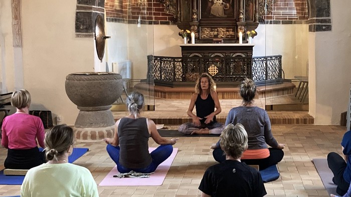 En gruppe af kvinder sidder på yoga-matser i en rummelig hal.