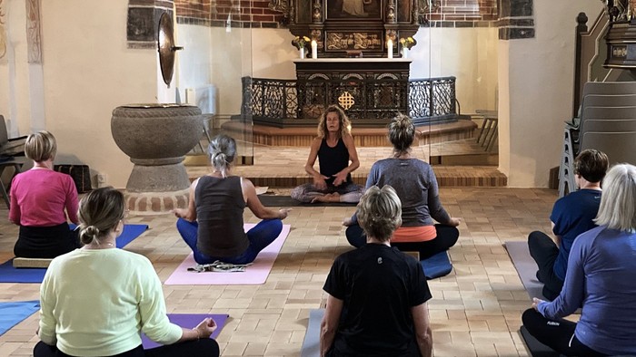 En gruppe af kvinder sidder på yoga-matser i en rummelig hal.