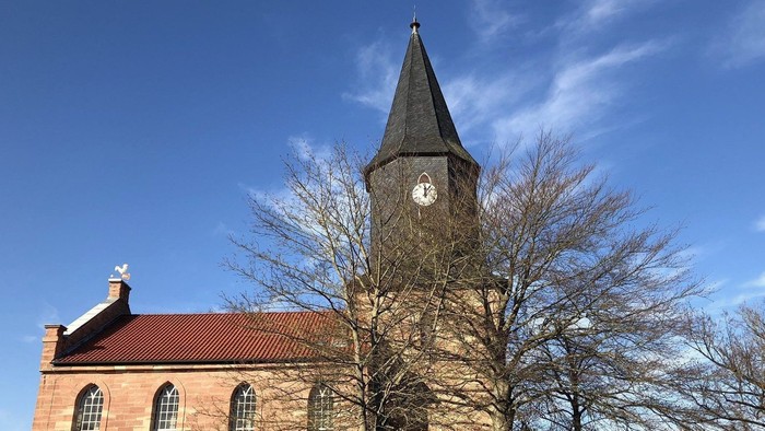 Kirchturm mit Uhr und Kirche im Hintergrund unter blauem Himmel