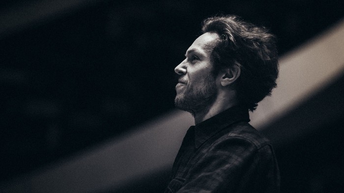 Ein konzentrierter Pianist spielt unter dramatischer Bühnenbeleuchtung das Keyboard, eingefangen in einem stimmungsvollen Porträt.