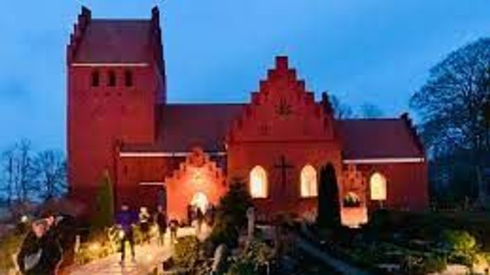 En rød kirke med spisse tårne og en gruppe mennesker ude foran.