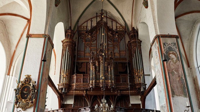 Historische große Pfeifenorgel in einem prunkvollen, gewölbten Kircheninnenraum mit hölzernen Kirchenbänken und dekorativen Wandmalereien.