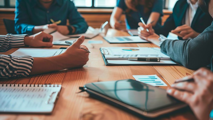 En gruppe af mennesker sidder ved et bord og arbejder med tablets og noter.