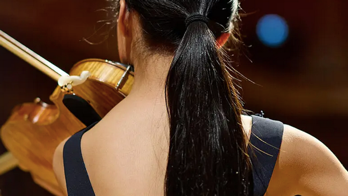 Eine Person, die auf der Bühne Geige spielt und lange Haare zurückgebunden hat.