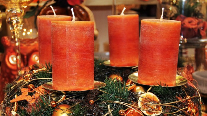Drei orange Kerzen auf grünem Kranz mit Weihnachtsdekoration