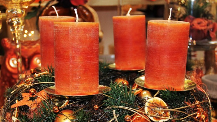 Drei orange Kerzen auf grünem Kranz mit Weihnachtsdekoration
