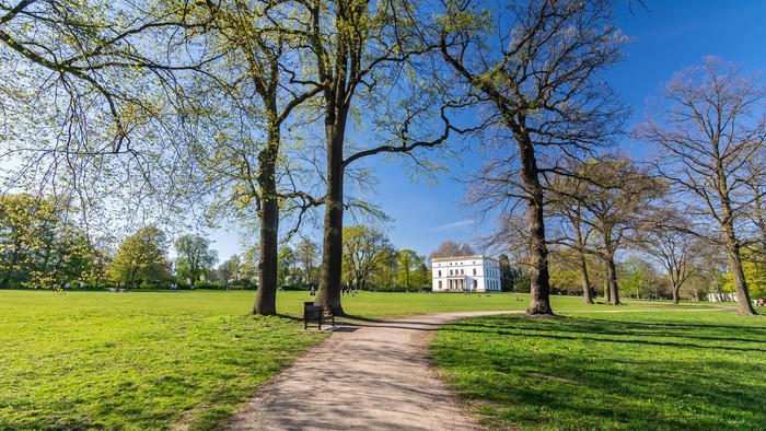 En smuk park med en sti, træer og et stort hus i baggrunden