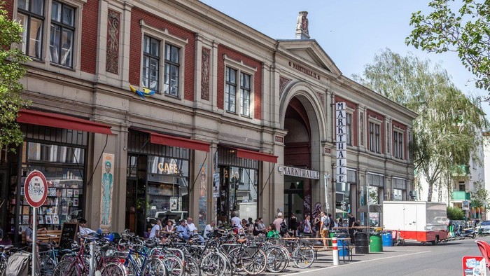 Vor einem großen Gebäude stehen viele Fahrräder und Menschen sitzen draußen.