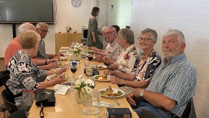 En gruppe ældre personer sidder sammen ved et bord og spiser.