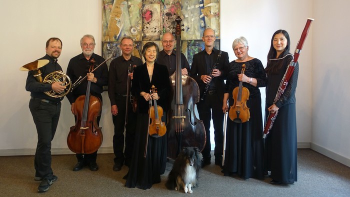 Musiker posieren mit Instrumenten, Hund im Vordergrund.