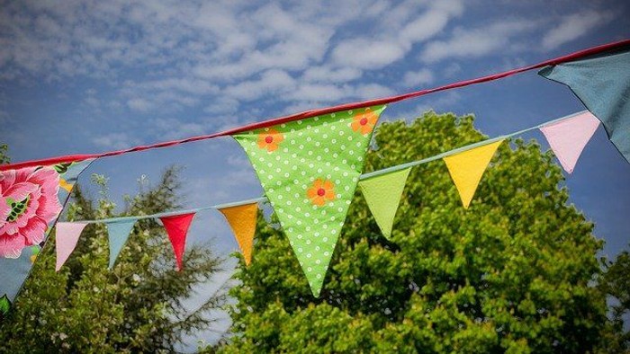 Colorful triangular flags strung across, with trees and blue sky in background