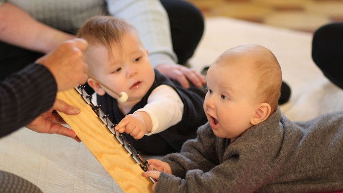 To barn spiller med et gult legetøj, mens en voksende sitter ved siden af dem