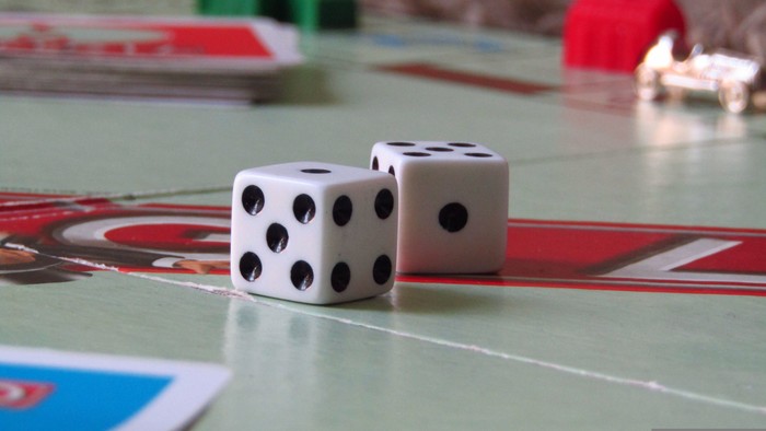 Zwei Würfel liegen auf einem Brettspiel mit bunten Wegen und verstreuten Spielkarten in der Nähe.