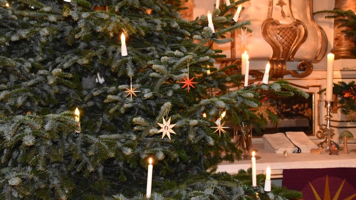 Ein Weihnachtsbaum mit Kerzen und Sternen, davor ein Kamin mit Dekoration