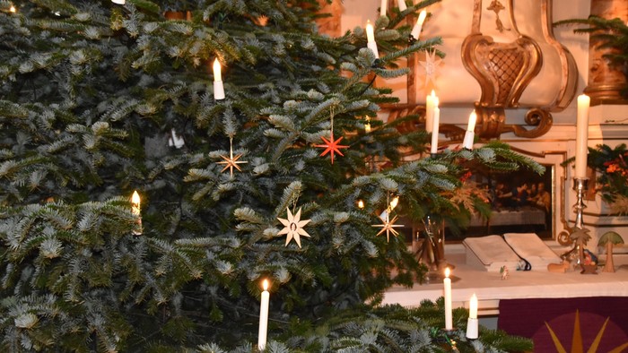 Ein Weihnachtsbaum mit Kerzen und Sternen, davor ein Kamin mit Dekoration