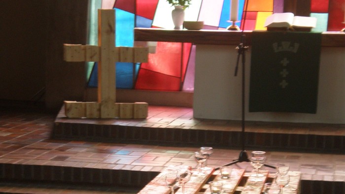 Ein langer Tisch mit Gläsern und Kerzen in einem Raum mit buntem Glasfenster