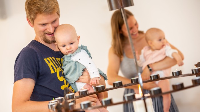 En mand træner på cykel med sit barn i armene, mens en kvinde med et andet barn træner på en cykel bagved.