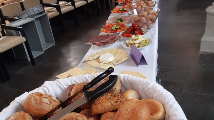 Ein großer Korb mit Brötchen steht auf einem Tisch mit verschiedenen Speisen.