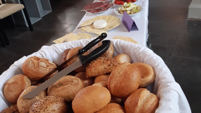 Ein großer Korb mit Brötchen steht auf einem Tisch mit verschiedenen Speisen.