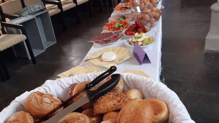 Ein großer Korb mit Brötchen steht auf einem Tisch mit verschiedenen Speisen.