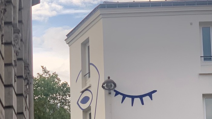 En blå og hvid tegnelse af et øje og en snak på siden af et hvidt bygning.