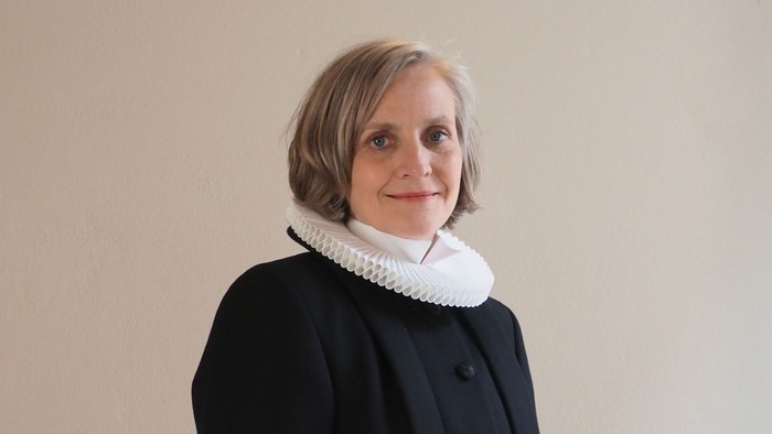 Kvinde i lang sort kappe med hvid krage og ærmbånd.