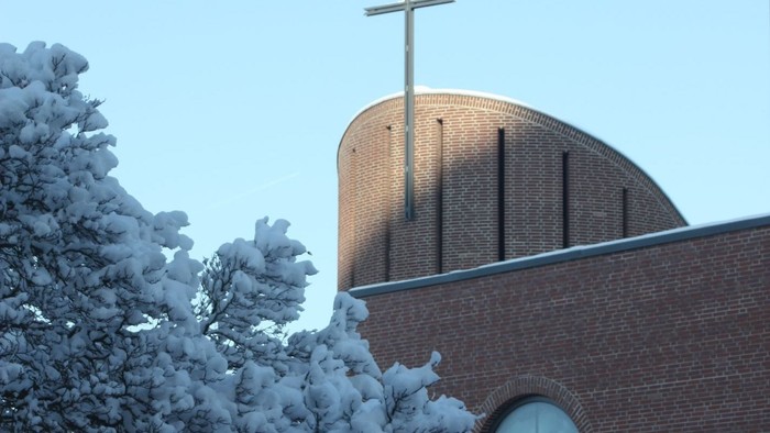 Schneebedeckte Kirche mit Kreuz auf dem Dach und Uhr an der Seite.
