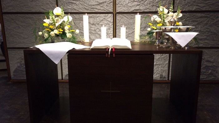 Altar mit Kerzen, Blumen und einem aufgeschlagenen Buch