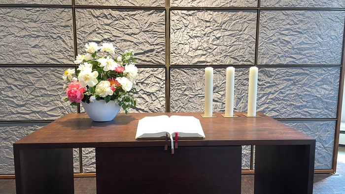 Blumenvase und Buch auf Altar vor grauer Wand