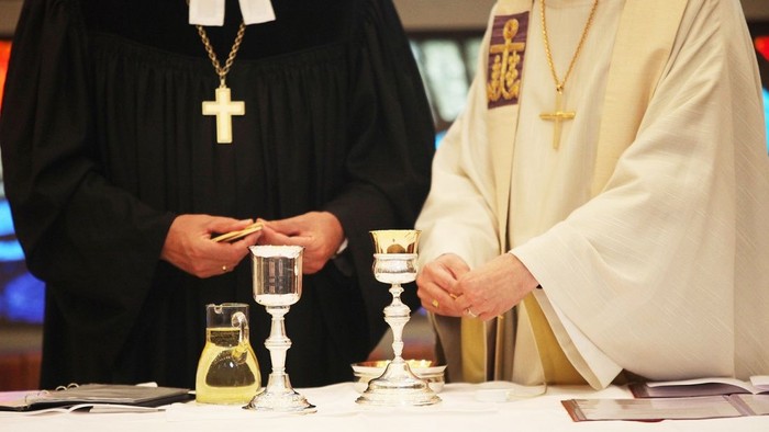 Zwei Priester in liturgischer Kleidung bereiten das Abendmahl vor