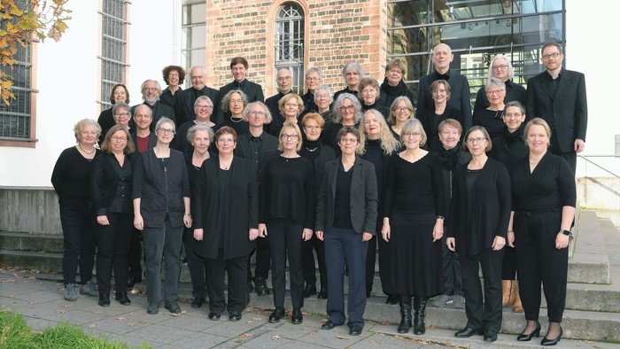 Ein offizielles Gruppenfoto eines Chors oder Vokalensembles in schwarzer Kleidung im Freien.