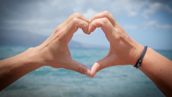 Zwei Hände bilden ein Herz vor dem Meer und dem Himmel
