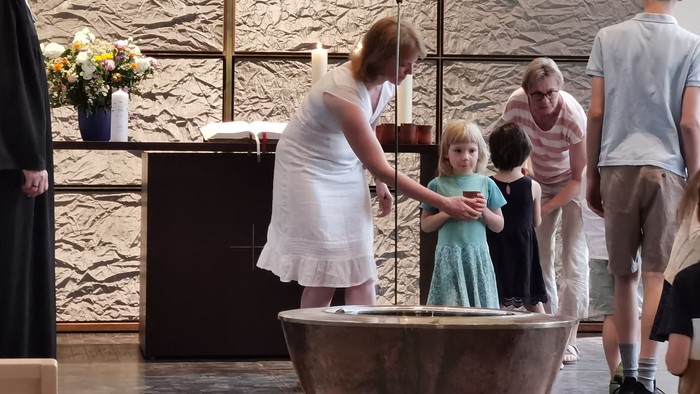 Ein Kind wird in einer Kirche getauft, während Familie und Geistliche am Taufbecken anwesend sind.