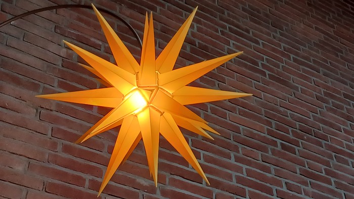 Eine leuchtende orangefarbene Sternlampe an einer Ziegelwand