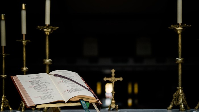 Geöffnetes religiöses Buch mit Kerzen und verzierten Kreuzen auf einem Tisch in einer feierlichen Umgebung.