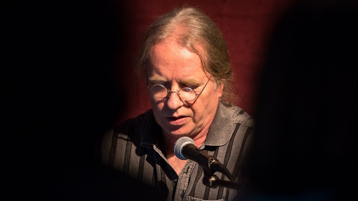 Eine Person spricht mit konzentriertem Gesichtsausdruck in ein Mikrofon auf der Bühne.